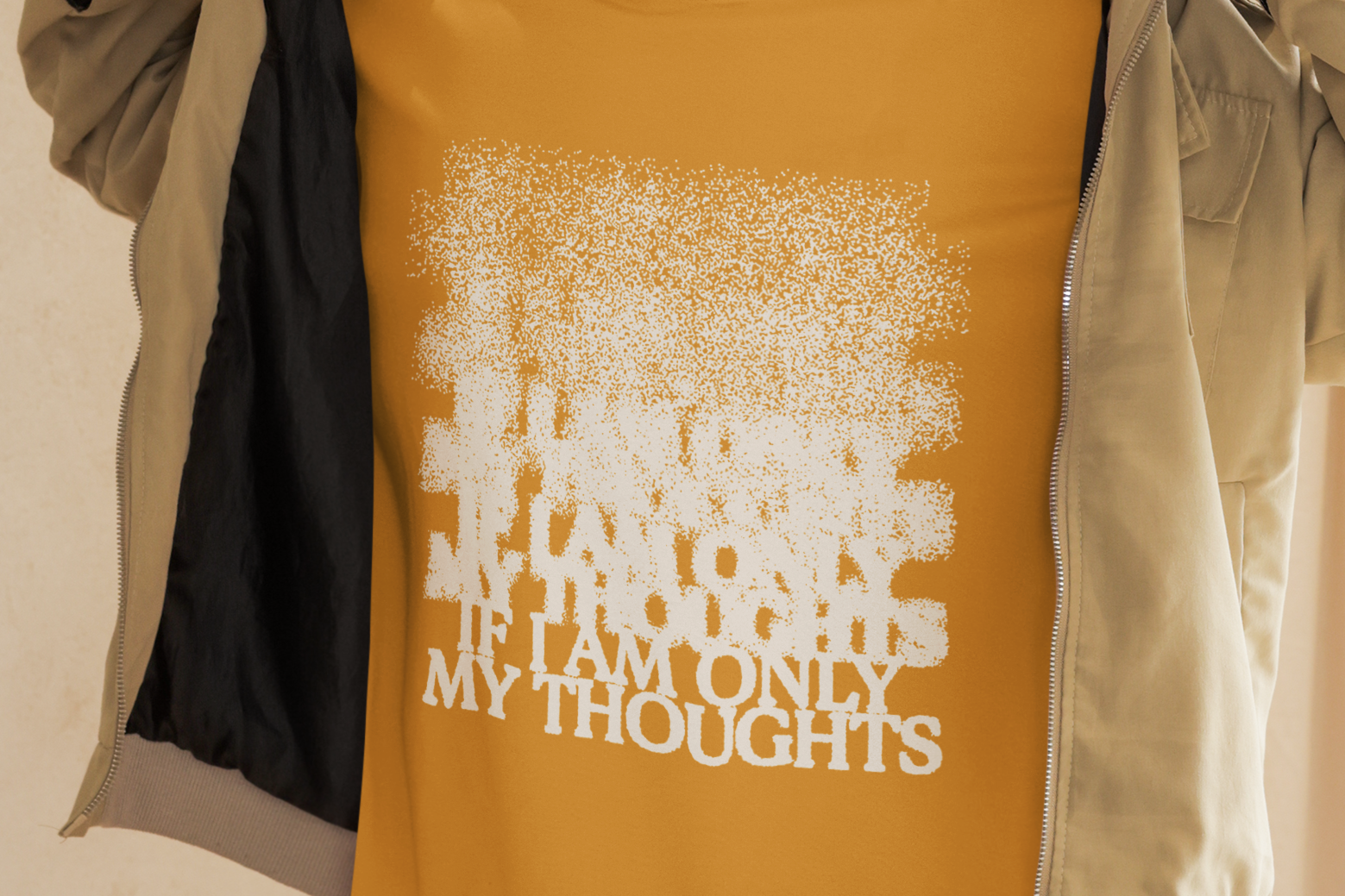 Person wearing a mustard yellow t-shirt with text, standing indoors against a neutral background